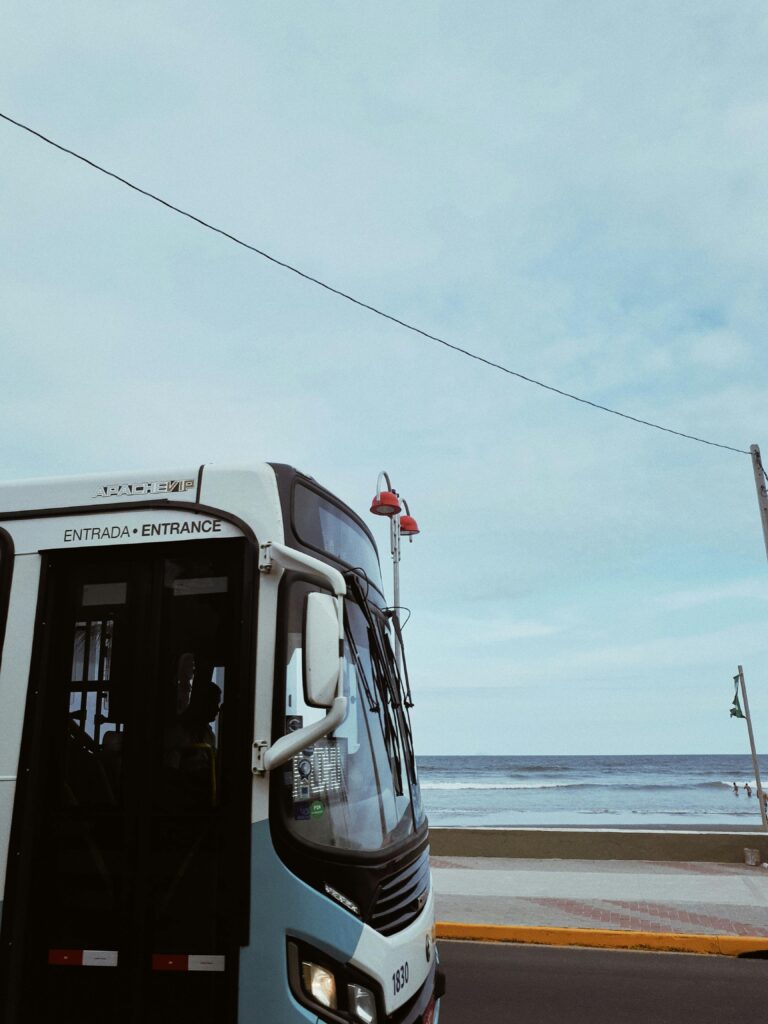 A public bus travels along a coastal road on a cloudy summer day, capturing the essence of travel.